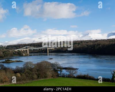 View across Menai Strait to Menai Suspension Bridge with snow covered Carneddau Mountains in the background on bright sunny winter's day Stock Photo