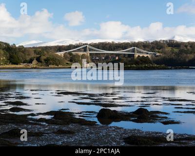 View across Menai Strait to Menai Bridge and Church Island  with snow covered Carneddau Mountains in the background on bright sunny winter's day Stock Photo
