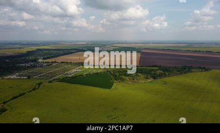 Green and yellow agricultural farm fields, fast moving shadows on the earth from white clouds in sky on a summer day. Agricultural panoramic landscape. Agrarian plantations scene. Aerial drone view. Stock Photo
