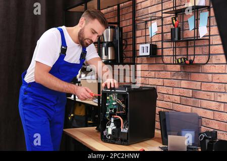 Repairman with screwdriver fixing coffee machine at table indoors Stock Photo