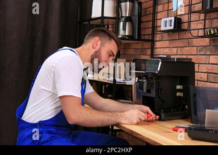 Repairman with screwdriver fixing coffee machine at table indoors Stock Photo