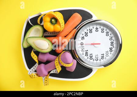 Scales, healthy food, dumbbells and measuring tape on yellow background, top view Stock Photo