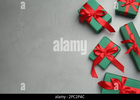 Many green gift boxes with red bows on light grey table, flat lay. Space for text Stock Photo