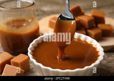 Taking tasty salted caramel with spoon from bowl at table, closeup Stock Photo