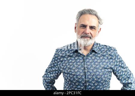 Studio shot of an older bearded grey-haired man in a blue patterned button-up shirt with hands on his waist. Smiling. Isolated on a white background. High-quality photo. Stock Photo
