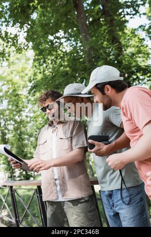 young guide in sunglasses and headset holding map near interracial travelers wearing sun hats in city park,stock image Stock Photo