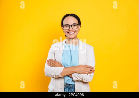 Focused successful brunette mixed race woman, wearing stylish casual clothes, hr manager, real estate agent, holds and sign documents, concentrated looks at them, stand on isolated yellow background Stock Photo