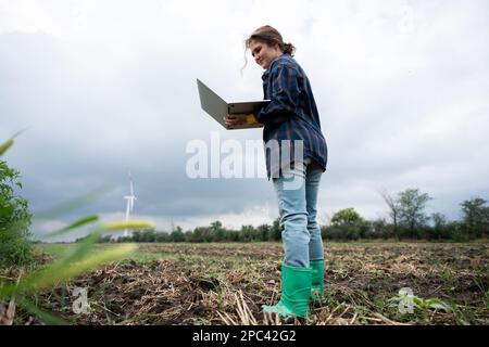 Farmer with laptop on the field. Wind turbines on a horizon. Smart sustainable farming and agriculture digitalization Stock Photo