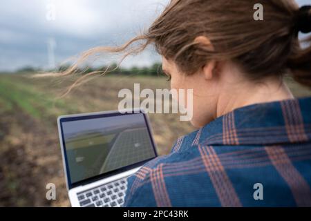Farmer with laptop on the field. Wind turbines on a horizon. Smart sustainable farming and agriculture digitalization Stock Photo