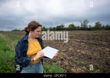 Farmer with laptop on the field. Wind turbines on a horizon. Smart sustainable farming and agriculture digitalization Stock Photo