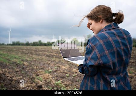Farmer with laptop on the field. Wind turbines on a horizon. Smart sustainable farming and agriculture digitalization Stock Photo
