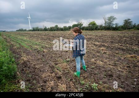Farmer with laptop on the field. Wind turbines on a horizon. Smart sustainable farming and agriculture digitalization Stock Photo