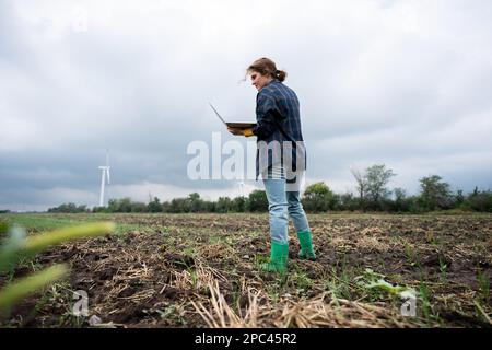Farmer with laptop on the field. Wind turbines on a horizon. Smart sustainable farming and agriculture digitalization Stock Photo