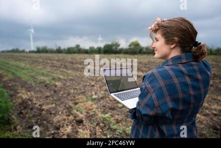 Farmer with laptop on the field. Wind turbines on a horizon. Smart sustainable farming and agriculture digitalization Stock Photo