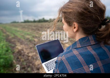 Farmer with laptop on the field. Wind turbines on a horizon. Smart sustainable farming and agriculture digitalization Stock Photo