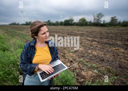Farmer with laptop on the field. Wind turbines on a horizon. Smart sustainable farming and agriculture digitalization Stock Photo