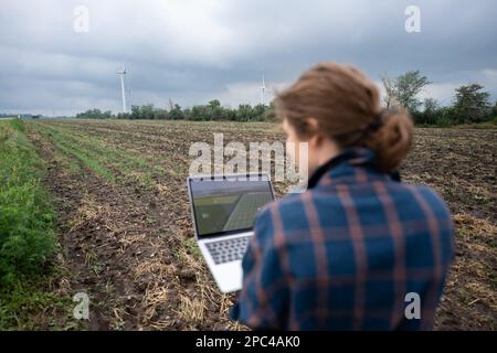Farmer with laptop on the field. Wind turbines on a horizon. Smart sustainable farming and agriculture digitalization Stock Photo