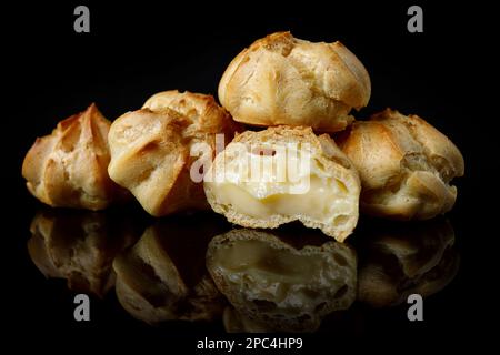 Profitroli cakes on black mirror with reflection, close-up Stock Photo