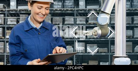 Warehouse manager with digital tablet controls robot arm Stock Photo