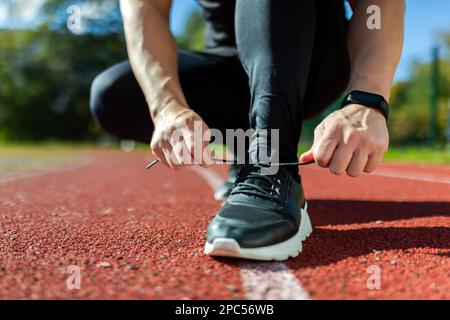 Close-up photo of a man's hand tying shoelaces at a sports stadium, a runner before starting a run and training, on a sunny day. Stock Photo