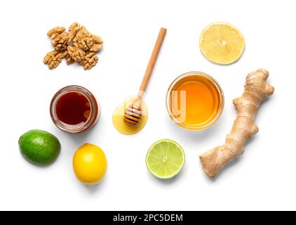 Composition of jars with honey, nuts, lemon, lime and ginger on isolation. Honey in bowls, dipper and fruits on a white background. Stock Photo