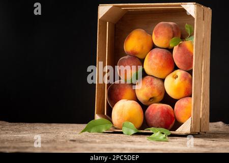 Peaches in a box on a wooden background top view. Fresh fruits on a vintage background. Peaches on a wooden background. Summer fruits in a wooden box. Stock Photo
