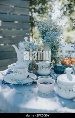 The aesthetic table set with white tea cups with blue flowers in nature. Stock Photo