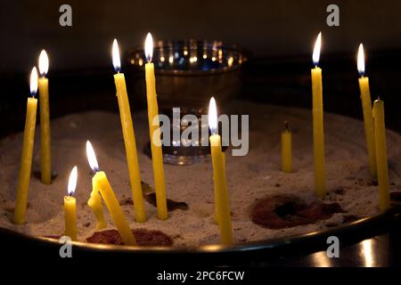 Many yellow candles burning in a church as symbol of belief and hope Stock Photo