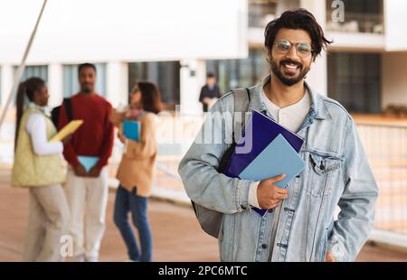 Smiling young indian male student with beard in casual and glasses with notebooks studying at university Stock Photo