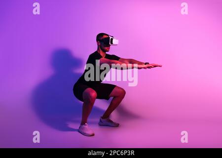 Black Man Wearing VR Headset Exercising Doing Squats, Purple Background Stock Photo