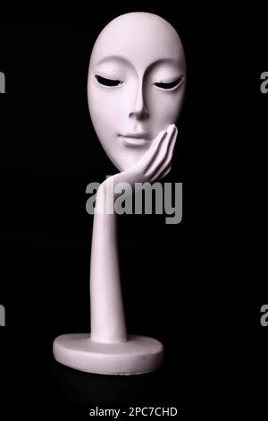 White mask resting on a hand on a black background Stock Photo