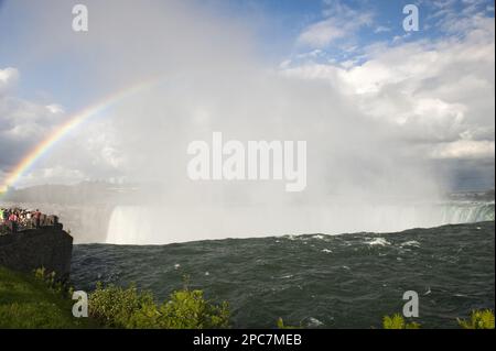 Rainbow forming in spray over waterfall, with tourists on viewing platform, Horseshoe Falls, Niagara Falls, Niagara River, Ontario, Canada Stock Photo