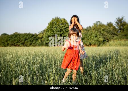 two girls in dresses playing with each other the evening grass field Stock Photo