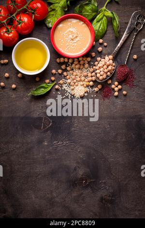 Hummus ingredients. Chickpea, tahini, olive oil, sesame seeds, sumac, herbs on dark rustic wooden background. Space for text. Set of ingredients for Stock Photo