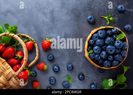 Fresh organic blueberry and strawberry with mint leaves in mini basket on vintage dark table. Concept of healthy eating. Top view, copy space. Stock Photo