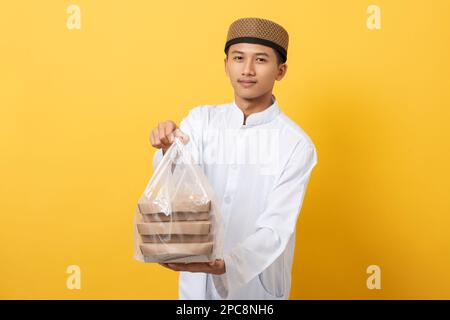 Young handsome asian muslim man giving alms or charity standing over orange background. happy ramadan and eid al-fitr. Stock Photo