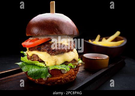 Burger with double meat, cheese and vegetables. French fries, sauce. Black background Stock Photo