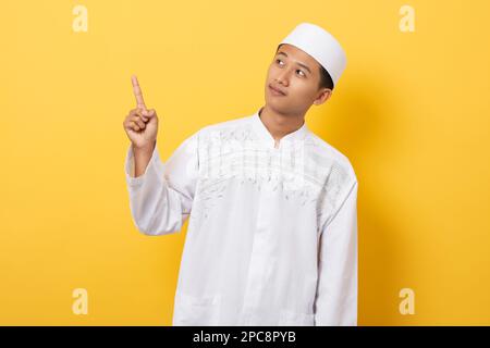 Young handsome asian muslim man standing over orange background pointing to the side with fingers Stock Photo