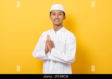 Young handsome asian muslim man gesturing greetings during ramadan isolated on orange background. happy ramadan and eid al fitr. Stock Photo