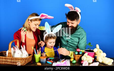 Easter holiday. Mother, father and son painting eggs. Happy family preparing for Easter. Cute child boy and parents in bunny ears. Easter Family Stock Photo