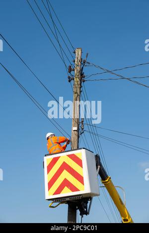 Telecommunications engineer working on wires on a telegraph pole. Telephone or broadband repairs being carried out at height from lift platform Stock Photo