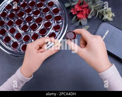 Closeup of young woman taking communion the wine symbol of Jesus Christ blood in small cups on black background. Easter Passover and Lord Supper conce Stock Photo