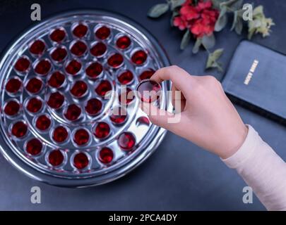 Closeup of young woman taking communion the wine symbol of Jesus Christ blood in small cups on black background. Easter Passover and Lord Supper conce Stock Photo