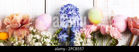 Spring bouquet of daffodils, hyacinths, roses, tulips with colorful easter eggs on a white wooden background. Happy Easter concept. Greeting card, ban Stock Photo