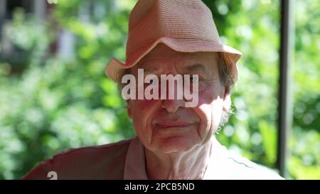 One fun Senior man portrait face changing expression. Older person wearing hat smiling at camera outdoors. Charismatic elder person Stock Photo
