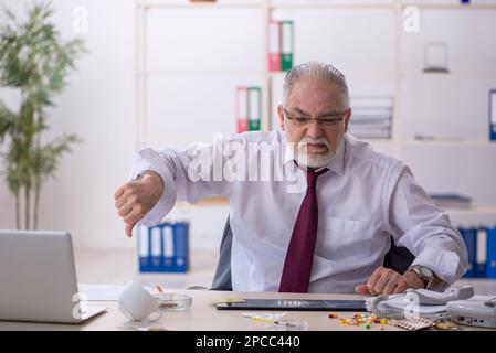 Old male drug addicted employee sitting at workplace Stock Photo