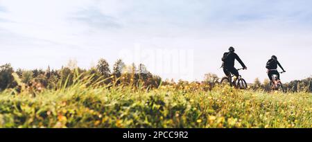 Young couple man and woman bicyclists with backpacks riding under sunset light at the early warm autumn time. Active sport people concept image Stock Photo
