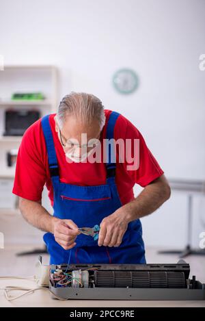 Old male repairman repairing air-conditioner Stock Photo
