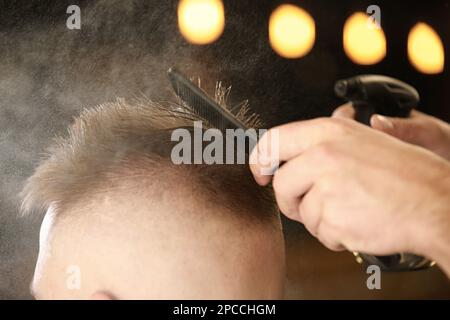 Close up of unrecognisable hairdresser of men's hairstyles makes a new stylish haircut, sets the hair with a spray and comb for a client in barbershop Stock Photo
