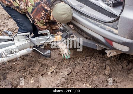A man checking the hitch mechanism on a car trailer in bad weather. Stock Photo